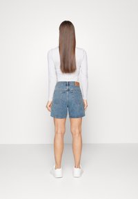 Shorts de mezclilla de tiro alto, lavado azul claro y dobladillo sin terminar. Combinados con una blusa gris de manga larga y zapatillas blancas.