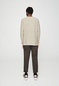 Haut beige clair à manches longues avec col rond, associé à un pantalon marron foncé fuselé et des baskets gris avec des semelles blanches.
