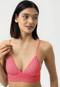 Vaaleanpunainen pitsinen bralette, jossa on kolmiomainen muoto ja säädettävät ohuet olkaimet. Siinä on kukkakuoseja ja aaltoileva reuna alareunassa.