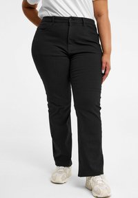 Mustat farkut suoran lahkeen muodossa, viiden taskun suunnittelulla, napin suljenta ja vyölenkkien kanssa, yhdistettynä vaaleanvärisiin urheilukenkiin.