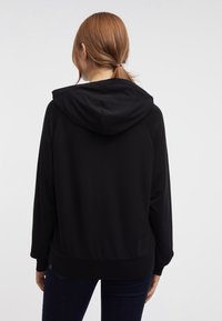 Sudadera con capucha negra de corte relajado, con puños y cintura de canalé. Textura suave, presenta una gran capucha y detalles de diseño mínimos.