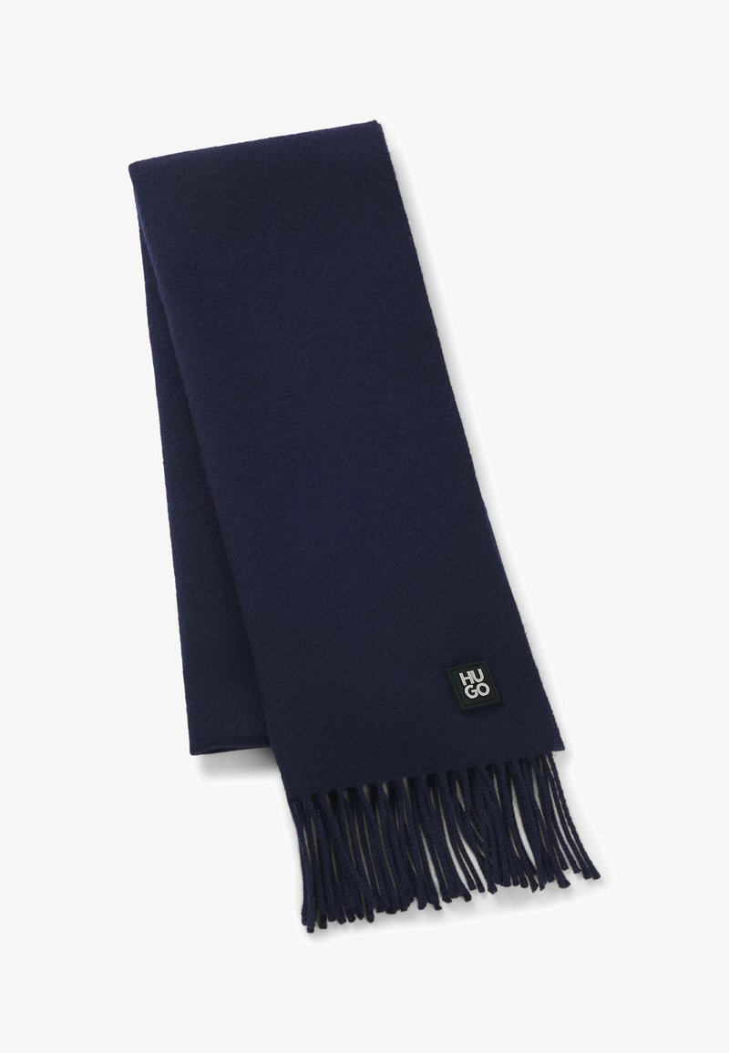 Sciarpa di lana blu navy con bordi frangiati, caratterizzata da un piccolo etichetta nera con il logo "HUGO" vicino a un'estremità. Morbido al tatto, di forma rettangolare.