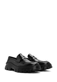 Zwarte leren loafers hebben een chunky rubberen zool met diepe groeven, een gladde afwerking en een decoratieve riem aan de voorkant.