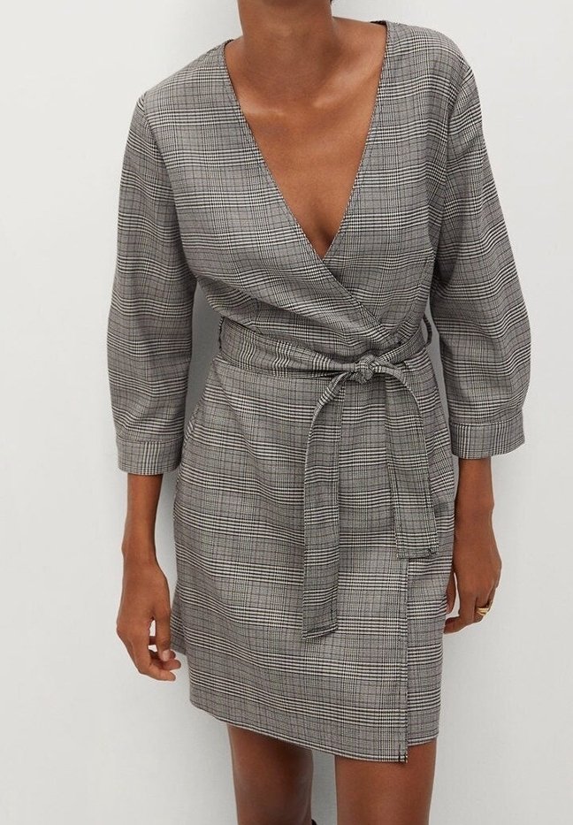 Szara w kratkę sukienka w stylu wrap z głębokim dekoltem w serek, trzy-czwartowymi rękawami i związanym w talii pasem. Materiał ma teksturowany, kratkowany wzór.