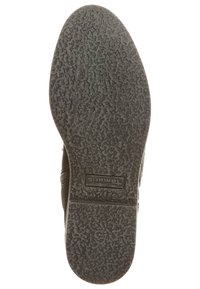 Semelle de chaussure en caoutchouc noir avec une surface texturée, arborant le logo de la marque "TOMS." Le design comprend une légère courbure au niveau des orteils et des motifs de bande de roulement prononcés.