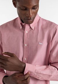 Camicia button-down rosa chiaro con una finitura testurizzata, caratterizzata da un piccolo logo di un cane ricamato in bianco sul petto e polsini con bottoni.