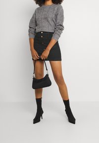 Šedý pletený svetr s texturovaným vzorem, černá džínsová mini sukně s předními knoflíky, úzká černá kabelka a černé kotníkové boty s špičatou špičkou.