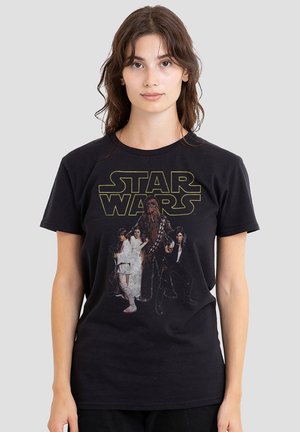 Young woman with long hair wearing a black Star Wars t-shirt featuring main characters and logo on a plain background.