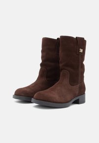 Bottes chevilles en suède marron avec une surface texturée, un bout rond, un petit talon, et une étiquette décorative sur le côté.