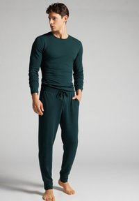 Donkergroene langarmshirt met ronde hals en slim fit, gecombineerd met tapered broek met een elastische tailleband en zakken.