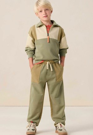 Olijf groene bicolor trainingspak met een ritskraag, contrasterend beige paneel en zakken. Zachte stof met elastische manchetten en tailleband.