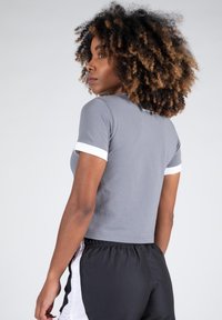 Grijze cropped shirt met witte accentkanten aan de mouwen, gecombineerd met zwarte shorts met witte netpanelen. Glad stof, slim-fitting ontwerp.