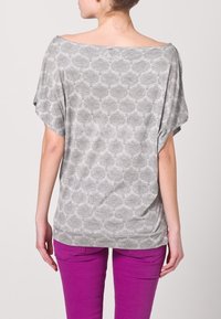 Top gris con patrón, de corte holgado y escote amplio, que cae sobre los hombros, combinado con jeans rosa ajustados, mostrando un estilo casual.