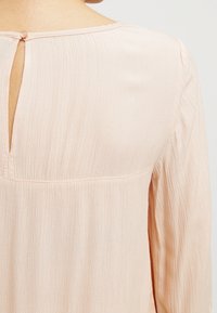 Ljusrosa blus med strukturerad tyg, med en nyckelhålsknäppning bak och en avslappnad passform. Mjuk drapering ger rörelse åt designen.