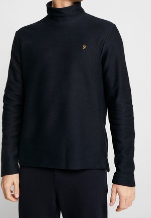 Navy textuurtrui met hoge kraag, lange mouwen, zijsplitten en een klein icoon op de borst. Zacht materiaal biedt een ontspannen pasvorm.