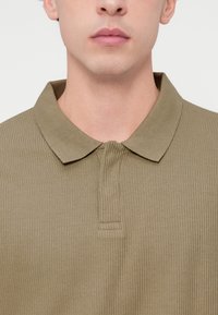 Πράσινο-ελαιί με ρίγες πόλο πουκάμισο με κλασικό γιακά, διαθέτει πατιλέτα με κουμπιά και υφή με ανάγλυφη τελείωμα.