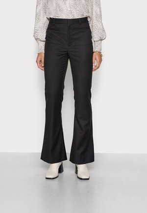 Czarne spodnie flare o gładkiej fakturze i dopasowanym kroju, zestawione z białymi botkami na obcasie, z kwadratowym obcasem i spiczastym czubkiem.