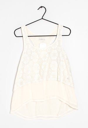 Witte mouwloze blouse met kanten overlay aan de bovenkant, ronde halslijn en asymmetrische zoom, hangend aan een zwarte hanger.