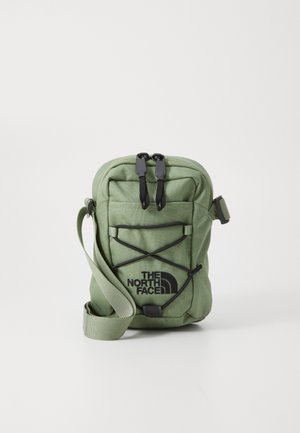 Lille grøn The North Face crossbody taske med sort logo, lynlåslomme foran, justerbar rem og elastisk snordetalje foran.