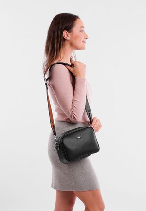 Černá kožená crossbody taška s strukturovaným designem, hnědým nastavitelným popruhem a stříbrným hardwarem. Má logo na přední straně.