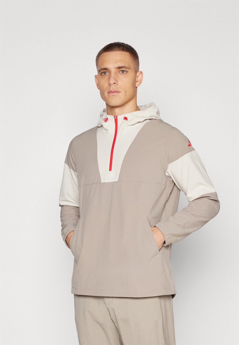 Lightweight, gray and cream jacket with a hood, half-zip front, side pockets, and red accents. Textured fabric with contrasting panels.