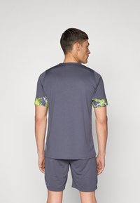 Grå atletisk t-shirt med korte ærmer, der har grønne og blå mønstrede detaljer. Blødt, åndbart stof, designet til aktiv brug.