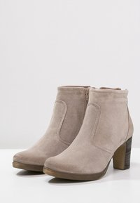 Bottines en suede beige avec un bout arrondi, fermeture éclair sur le côté et un talon épais texturé, présentant une finition lisse et des détails de couture minimaux.