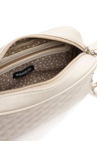 Borsa a tracolla beige con esterno sintetico trapuntato. Presenta una fodera interna a motivo stellato, tasche con zip e un accentuato attacco in metallo argentato.