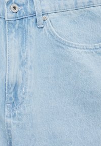 Světle modrá dením látka s jemnou texturou, s předním zapínáním na knoflík a zip a zakřiveným designem kapsy.