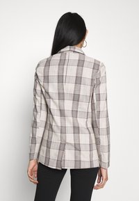 Blazer a quadri beige e marrone con una vestibilità strutturata, maniche lunghe e una fessura sul retro, realizzato in tessuto testurizzato.