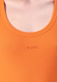 Camiseta de tirantes naranja con textura de acanalado que presenta un escote redondo y el logo bordado "BOSS" cerca del centro. Textura suave con un diseño ajustado.