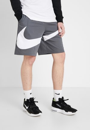 Persoon die grijze short draagt met een groot wit swoosh-ontwerp, zwart-witte Nike-sneakers, witte Nike-sokken en een zwart-wit bovenstuk.