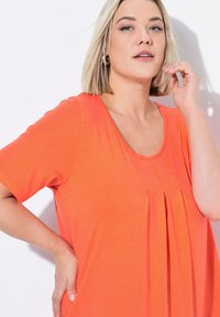 Oranžový krátký rukáv top s kulatým výstřihem a vertikálními záhyby v přední části. Vyrobeno z lehké, jemné tkaniny s hladkým povrchem.