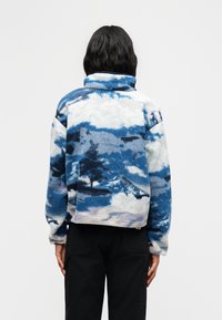 Φλις πουλόβερ με μοτίβο γαλάζιου και λευκού ορεινού τοπίου. Υψηλός γιακάς, κοντό σχέδιο και απαλή υφή.