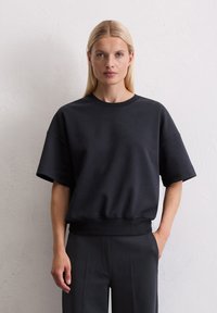 Zwarte sweatshirt gemaakt van zachte stof, met een ronde hals, korte mouwen en een relaxte pasvorm die bij de taille samenkomt.