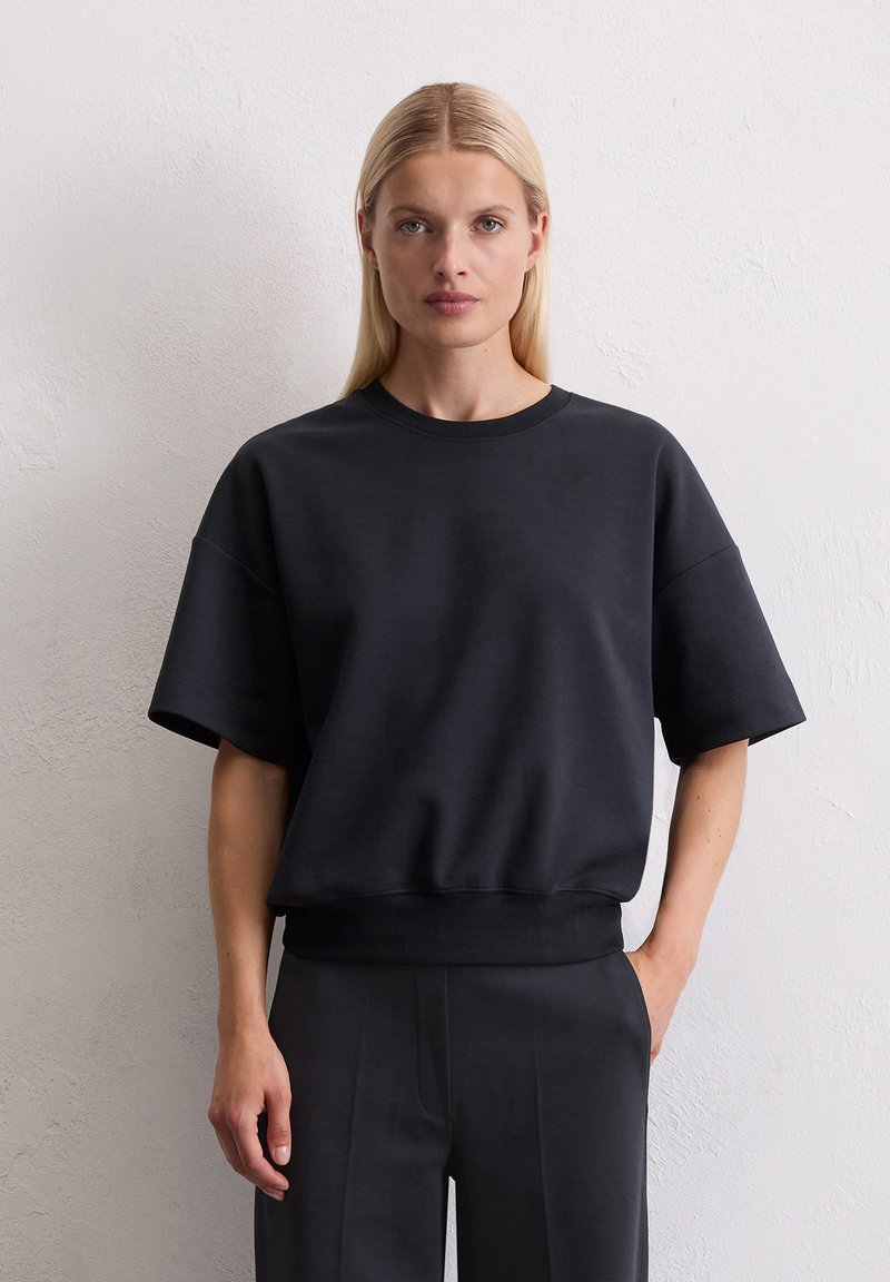 Zwarte sweatshirt gemaakt van zachte stof, met een ronde hals, korte mouwen en een relaxte pasvorm die bij de taille samenkomt.