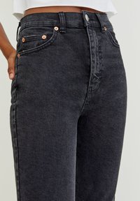 Jeans de mezclilla negra con forma ajustada, detalles en metal cobre y diseño de cinco bolsillos. Tela texturizada con un ligero brillo.