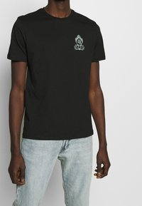 Czarny bawełniany t-shirt z okrągłym dekoltem, krótkimi rękawami oraz centralnym wzorem graficznym w bieli, z misternymi detalami.