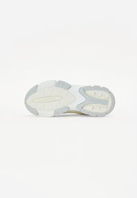Des chaussures avec une semelle en caoutchouc blanc texturé, présentant une combinaison d'accents crème et gris clair, ainsi qu'un motif de semelle pour une meilleure adhérence.