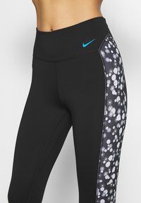 Černé sportovní legíny s vysokým pasem, které mají květinový potisk na panelu a malé modré logo Nike na přední straně.