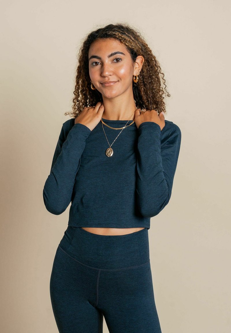 Námornícky cropped top s dlhým rukávom a priliehavými rukávmi, spárovaný s vysokými legínami v rovnakom odtieni; hladká textúra a minimálne detaily šitia.
