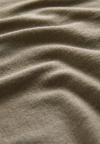 Detailní záběr měkké, béžové pleteniny, ukazující texturu a jemné záhyby.
