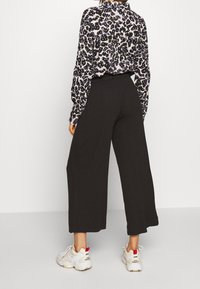 Pantalons noirs à jambes larges avec une texture côtelée, associés à un blouse à motifs présentant un imprimé léopard dans des tons de noir, blanc et violet.