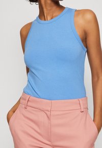 Ljusblå ribbad tank-top med rund halsringning och ärmlös design, tillsammans med ljusrosa skräddarsydda byxor med sidofickor.
