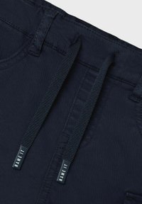 I pantaloni elasticizzati blu navy presentano una texture liscia, una cintura con cordino e dettagli con logo sulle estremità del cordino.