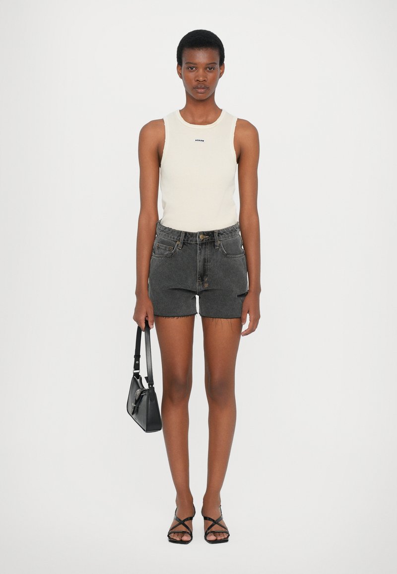 Top senza maniche beige chiaro, pantaloni shorts in denim neri con orlo sfrangiato, borsa nera e sandali neri con cinturini. Design semplice e aderente.