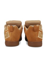 Et par brune suedestøvler med polstret beige inderside, brune gummisåler, hælpulltabs og stiliserede bogstavdesigns på siderne.