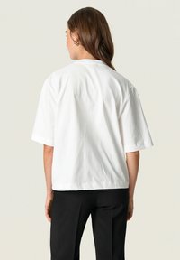 White cotton t-shirt with short sleeves and a relaxed fit. The back features smooth texture, rounded neckline, and basic design.