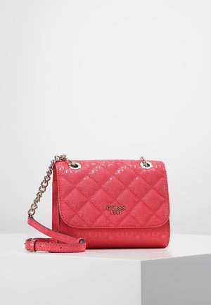 Sac bandoulière matelassé rouge avec bandoulière chaîne argentée et logo "GUESS 1981" sur le devant, présenté sur un piédestal blanc sur fond uni.