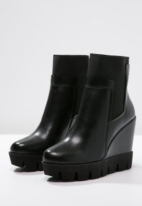 Botines de cuña de cuero negro con un acabado suave, paneles laterales elásticos y una suela gruesa y estriada para mayor agarre.